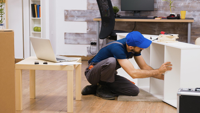 Professional worker in overalls consults furniture assembly instructions from laptop